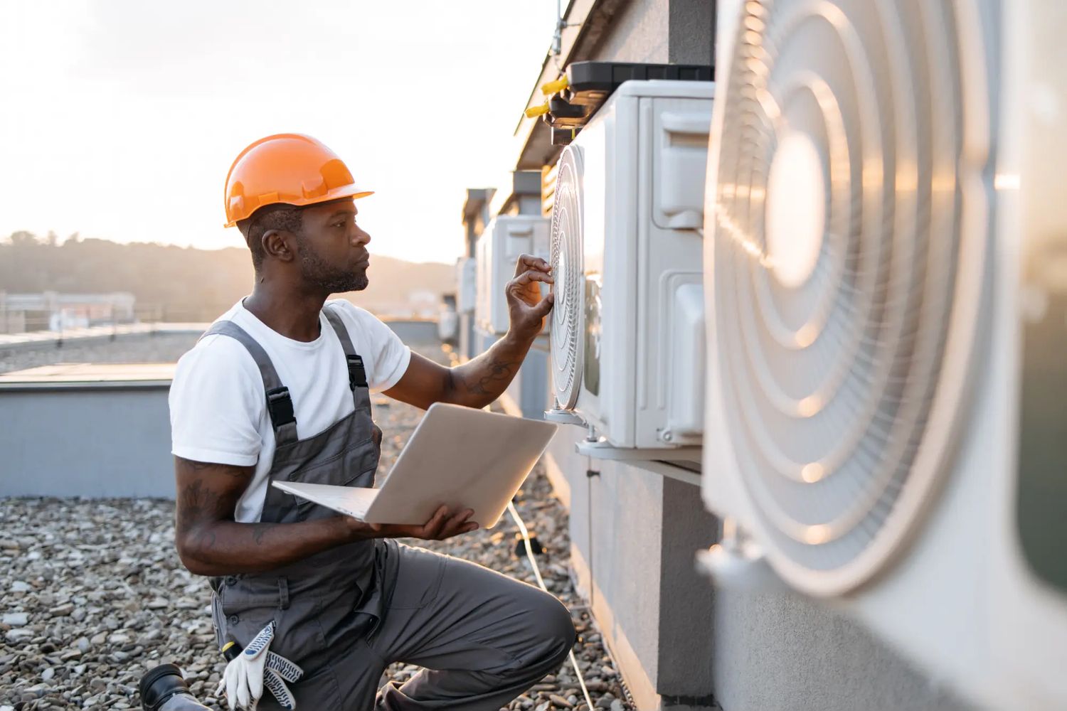 HVAC technician in a hard hat checking rooftop units with a laptop